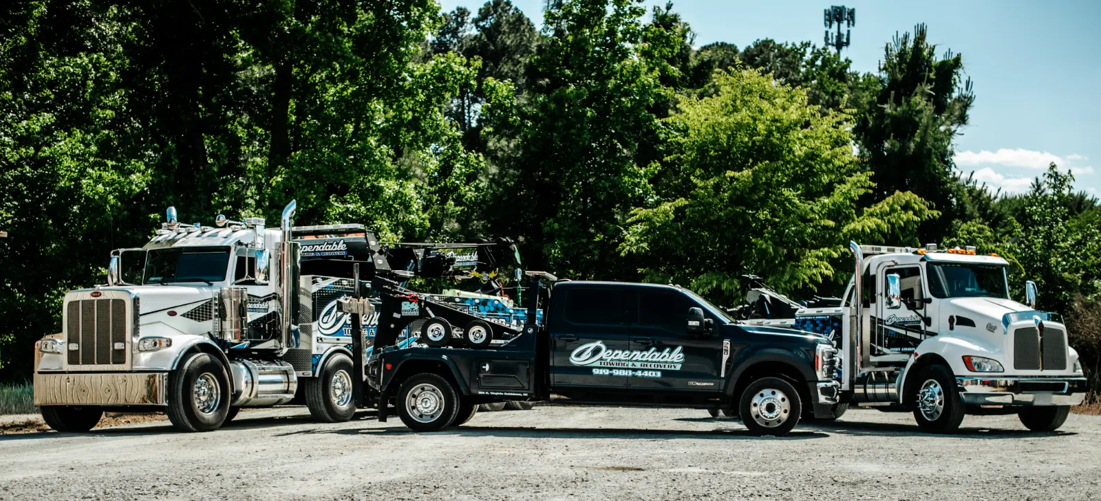 Dependable Towing & Recovery heavy rotator, pickup wrecker and medium wrecker parked side by side on a gravel lot