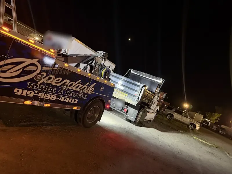 Dependable wrecker hooked to a dump truck at night